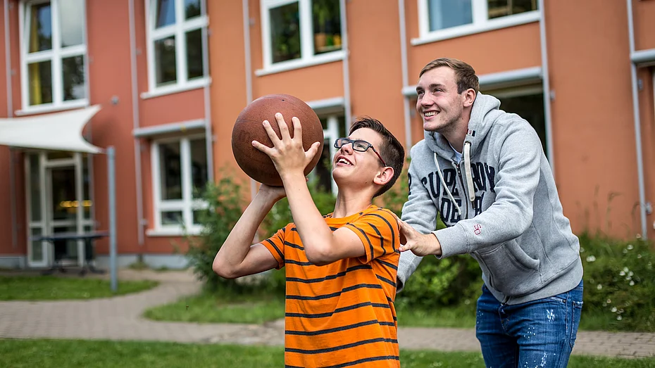 Freiwilliger unterstützt Kind beim Basketball